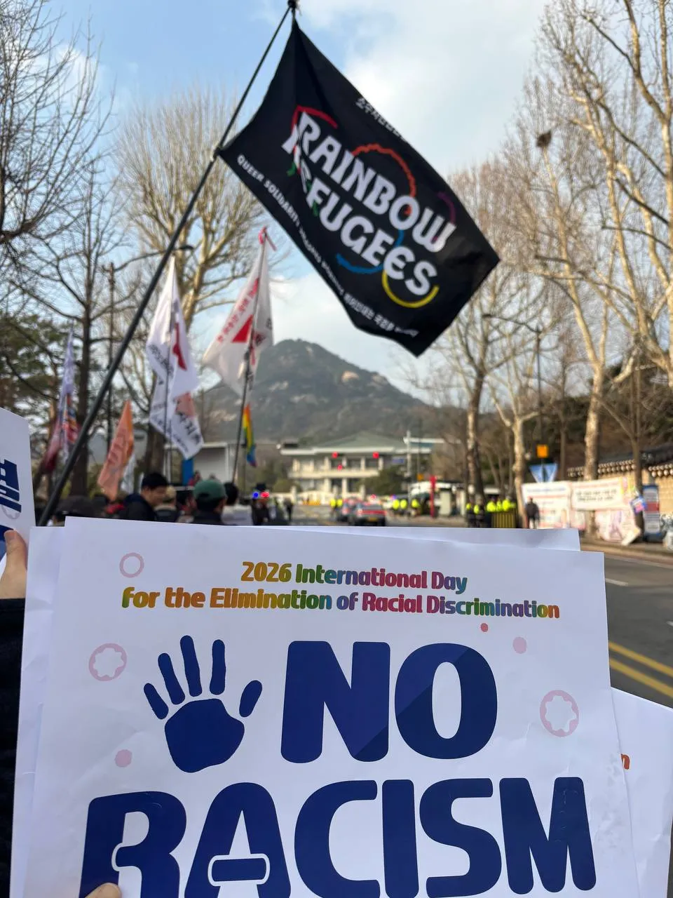 소수자난민인권네트워크의 깃발과 2026년 세계인종차별철폐의날 기념대회 피켓의 사진. 깃발에는 “Queer Solidarity Smashes Borders 퀴어 연대는 국경을 부순다”라는 문구가, 피켓에는 “NO RACISM”이라는 문구가 적혀 있다.