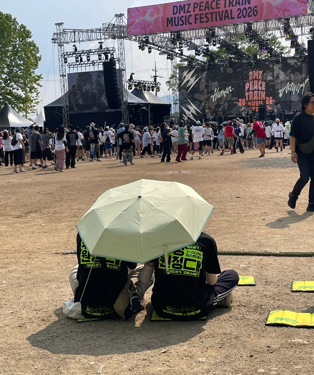 낮의 축제 현장 사진. 우산을 쓰고 컴포터블 존에 앉아 공연을 관람하고 있는 2명의 우정원정대원.