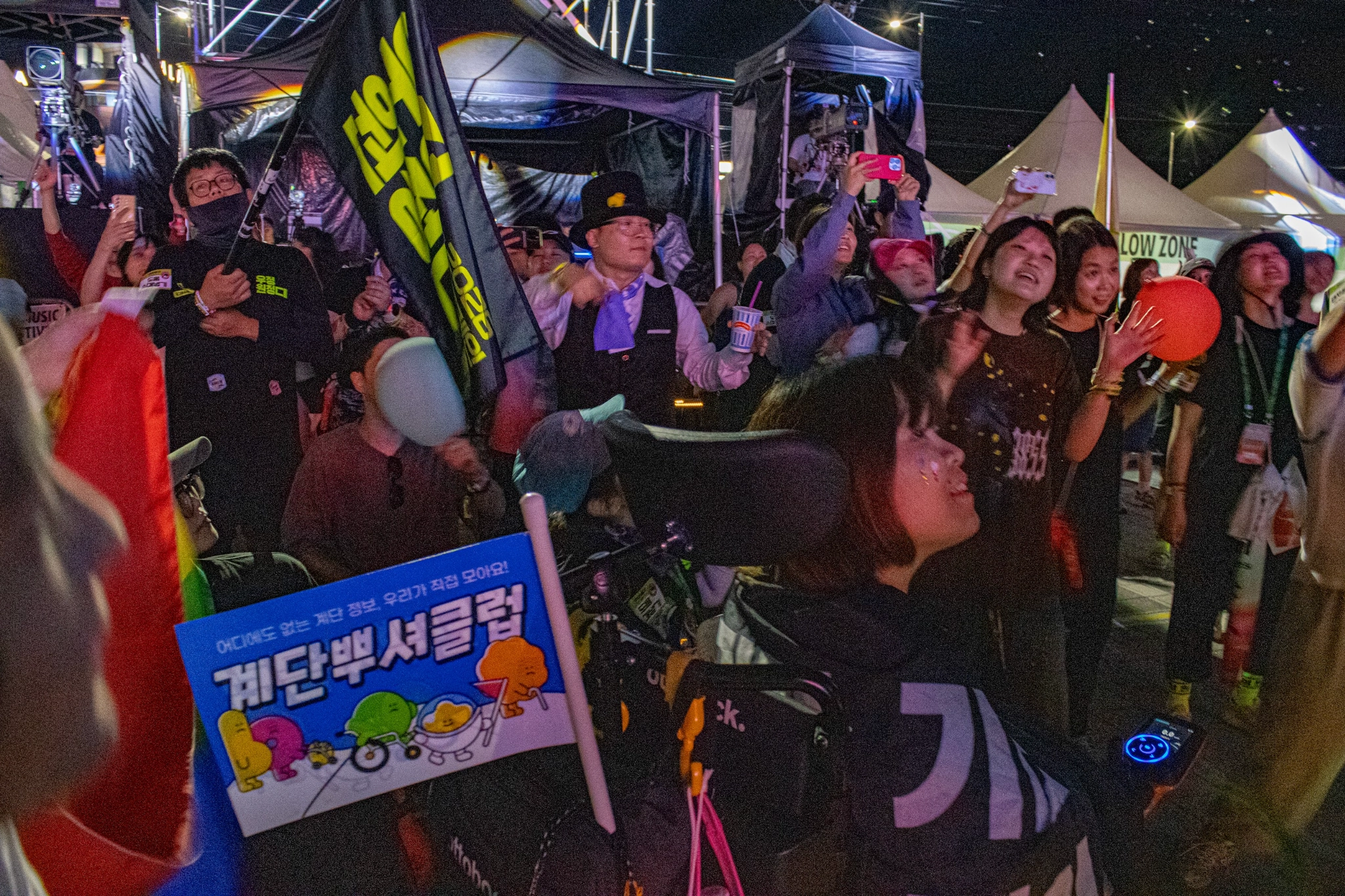 저녁의 축제 현장 사진. 컴포터블 존에 우정원정대를 포함한 다양한 관객이 무대를 바라보고 있다.